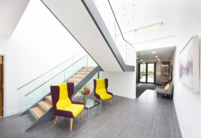 Spacious communal lounge with vibrant yellow wingback chairs situated under a modern staircase.