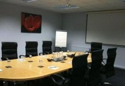 Professional meeting room featuring a long oval table, black executive chairs, and a projector screen.