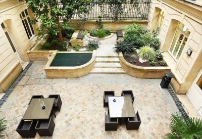 Sunlit interior courtyard with paved flooring, manicured plants, and outdoor seating.