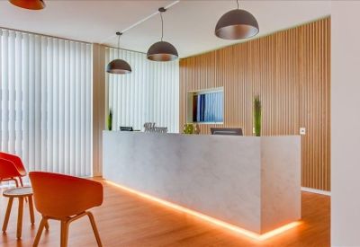 Reception area with a concrete-style front desk, wood-paneled walls, and orange guest chairs.