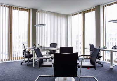 Bright corner office with multiple workstations and floor-to-ceiling windows with blinds.