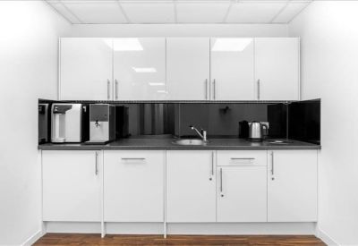Clean, modern kitchen area with white cabinetry and integrated coffee machines.