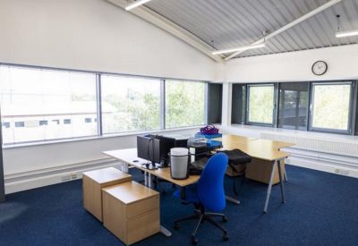 Bright corner office with blue carpet and a large window overlooking trees.