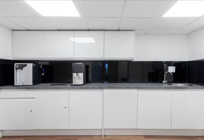 Modern communal kitchen area with white cabinetry and sleek black splashback.