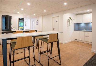 Modern breakroom area with high-top tables, wooden stools, and a small kitchen.