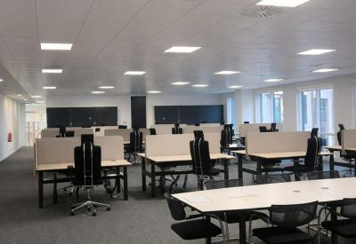 Spacious open-plan workspace with multiple rows of white desks and ergonomic black chairs.