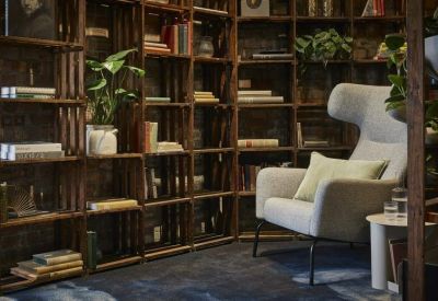 Cozy lounge area with a grey wingback chair and floor-to-ceiling wooden bookshelves.