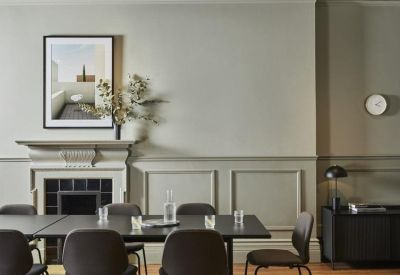Bright boardroom with a long black table, fireplace, and sage green panelled walls.