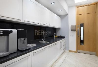 Modern office kitchen with white cabinetry, black countertops, and a coffee machine.