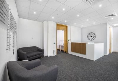Bright reception area featuring a white and wood desk, grey sofas, and a large analog wall clock.
