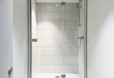 Modern walk-in shower with white vertical tiling and a glass door.