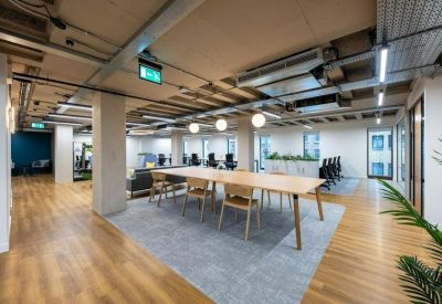 Bright workspace featuring large wooden desks, ergonomic chairs, and industrial ceilings.