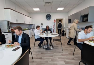 Modern communal kitchen and dining area with people eating at round tables.
