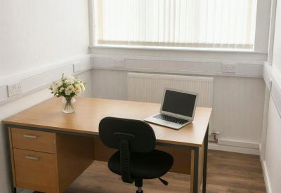 Private office suite with a wooden desk, black swivel chair, and floral arrangement.