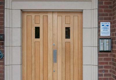 Main entrance with light wood double doors framed by a stone archway and brick walls.