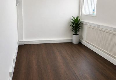 Bright, empty office space with dark wood-style flooring and a potted plant in the corner.