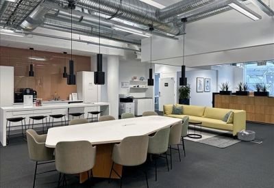Large breakout area with a communal dining table, modern sofa, and industrial ceiling.