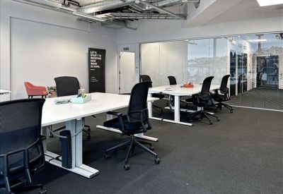 Spacious open-plan office with white height-adjustable desks and black ergonomic chairs.