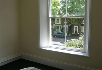 Private office with dark carpets and a large sash window overlooking a street.