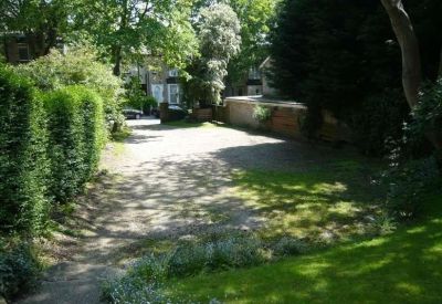 Paved outdoor area and driveway surrounded by mature green trees and hedges.