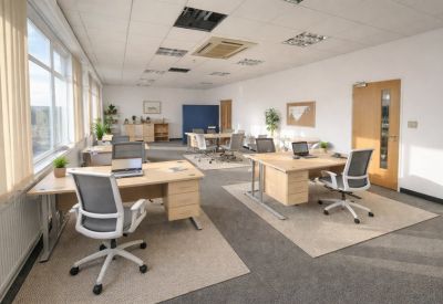Spacious coworking area with multiple desks, ergonomic chairs, and neutral carpeting.