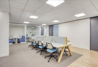 Modern coworking space featuring blue chairs, wooden-legged desks, and private booths in the background.