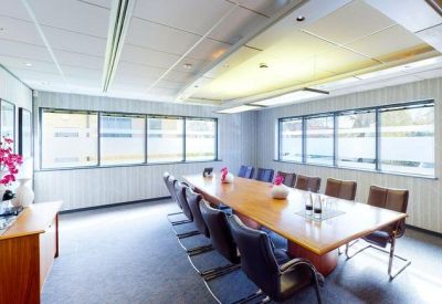 Spacious boardroom with a large wooden table, leather chairs, and ample natural light.