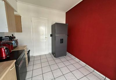 Kitchen area with tiled floors, a large grey refrigerator, and a bold red accent wall.