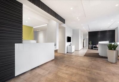 Bright reception area with a white front desk, dark textured feature wall, and wooden flooring.