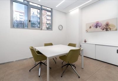 Minimalist four-person meeting room with a white table, green chairs, and floral wall art.