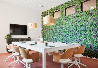 Meeting room with a large white table, wooden armchairs, and a vibrant green moss feature wall.