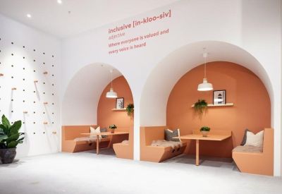 Modern breakout booths with arched orange walls and a wall-mounted definition of inclusive.