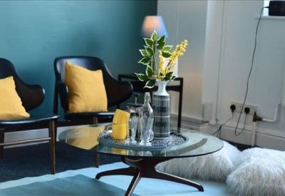 Stylish lounge area with teal feature wall, mid-century modern chairs, and yellow cushions.