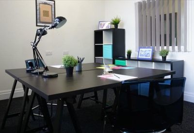 Modern four-person workspace with dark desks, green plants, and a stylish black desk lamp.