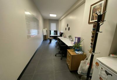 Narrow office corridor with long white desk surfaces, wooden storage, and a whiteboard wall.