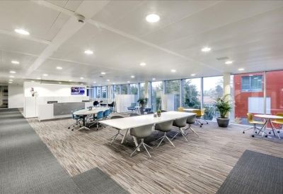 Spacious communal coworking area with long white tables and bright overhead lighting.