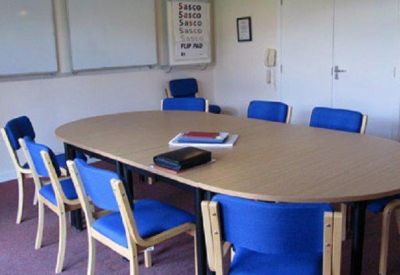 Meeting room featuring an oval wooden table and blue chairs.