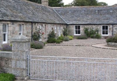 Courtyard view of stone buildings with a metal gate in the foreground.