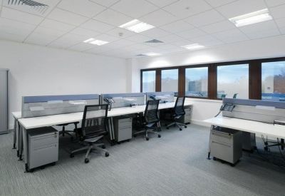 Modern open-plan office with rows of white desks and ergonomic black chairs.