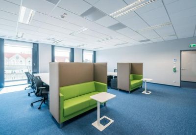 Open-plan office with desks and semi-private green sofas.