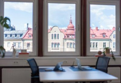 Bright workspace with desks and large windows overlooking red-roofed city buildings.