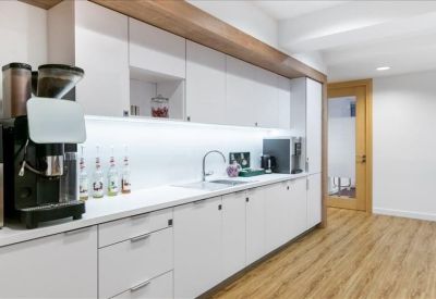 Modern office kitchen with white cabinetry, wooden accents, and an espresso machine.