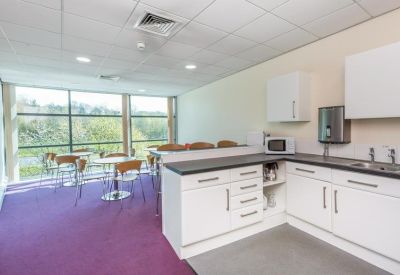 Bright communal kitchen and breakout area with purple carpet and large windows.