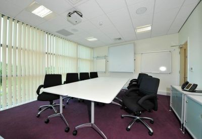 Professional meeting room with a large white table, black chairs, and a projector screen.