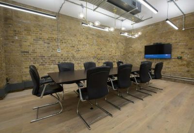 Professional boardroom featuring a dark wood table, black leather chairs, and an exposed brick wall.