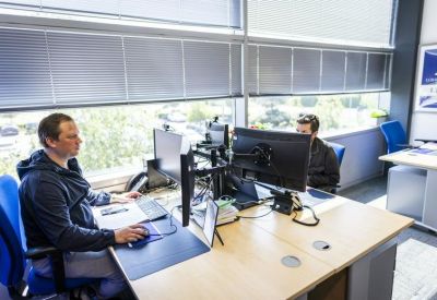 Office workspace with professionals working at desks near large windows.