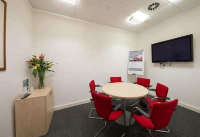 Small meeting room with a round table, red chairs, and a wall-mounted screen.