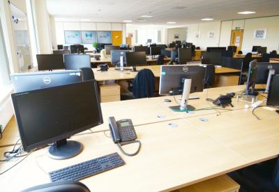 Bright open-plan office with rows of desks and desktop monitors.