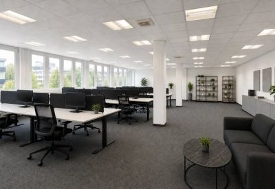 Bright open-plan office with rows of white desks, ergonomic black chairs, and large windows.