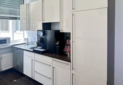 Modern office kitchen with white cabinetry, built-in coffee machine, and integrated appliances.